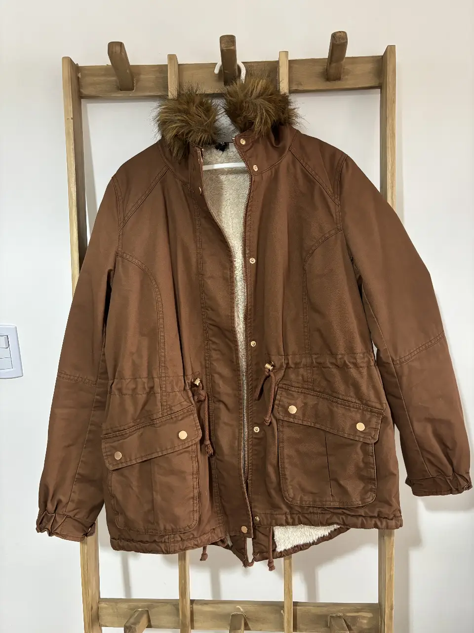 Campera marrón con capucha y detalles de piel sintética en el borde. Posee bolsillos delanteros y ajuste en la cintura. Ideal para el invierno. Se puede sacar el peluche de la capucha