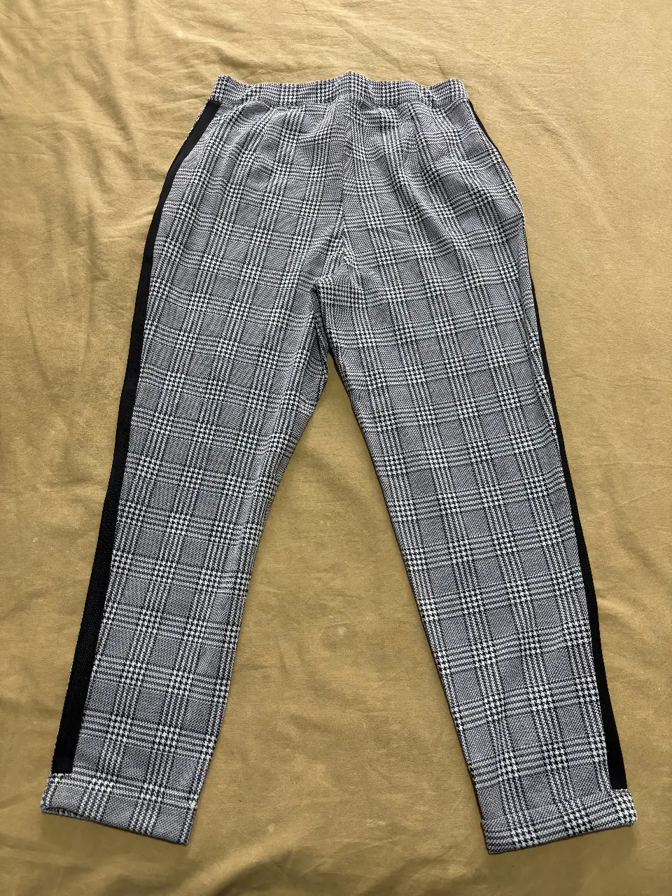 Pantalón sastrero de mujer con estampado a cuadros en tonos grises y negro. Diseño elegante con detalle de cinta negra en los laterales. Ideal para un look sofisticado y moderno.