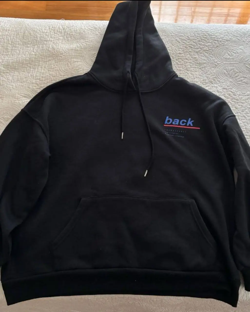 Buzo canguro negro con capucha y estampado "back" en azul y rojo. Diseño urbano y cómodo, ideal para un look casual y moderno. Perfecto para el día a día.