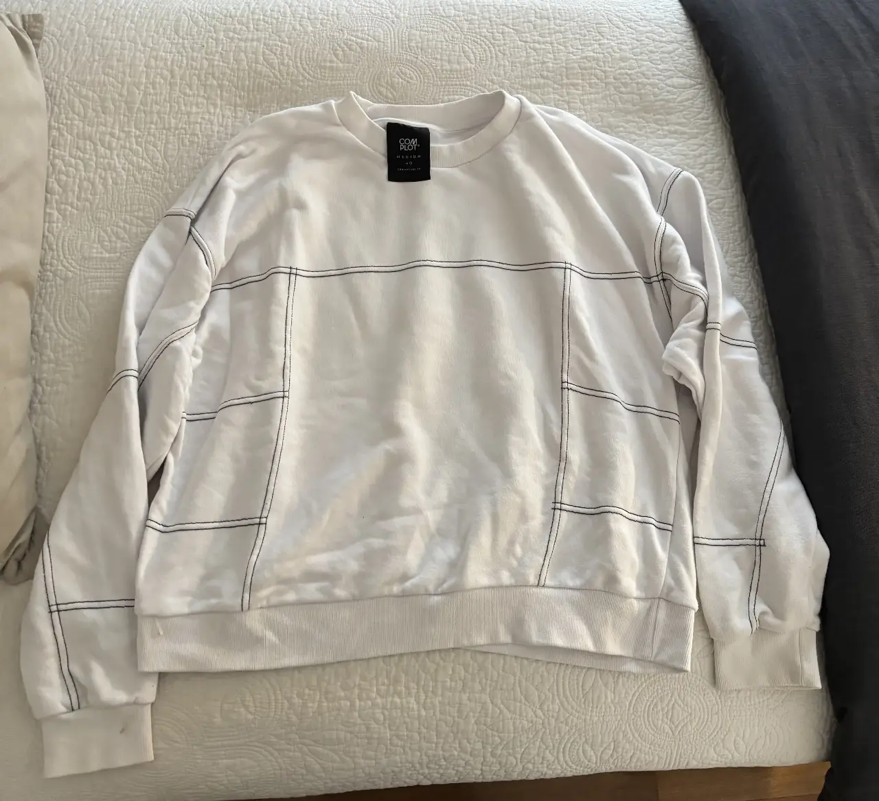 Buzo de cuello redondo blanco con detalles de costuras negras. Ideal para un look casual y moderno. Marca COMPLOT.