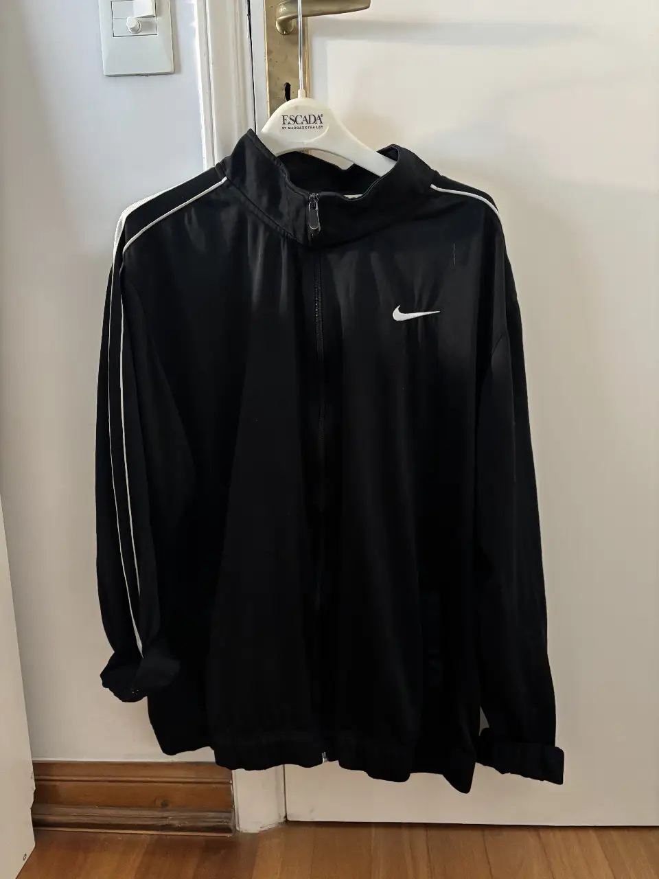 Campera deportiva Nike negra con detalles blancos. Ideal para entrenar o usar en el día a día. Con cierre y logo de la marca.