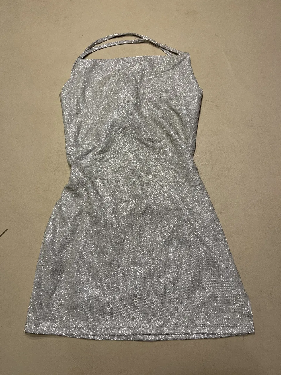 Vestido mini plateado con espalda descubierta y tiras finas. Ideal para fiestas y eventos especiales. impecable