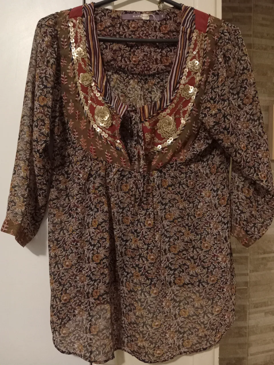 Blusa estampada con detalles de lentejuelas y bordados en el cuello. Posee mangas 3/4 y un diseño delicado y bohemio, ideal para un look casual o de salida.