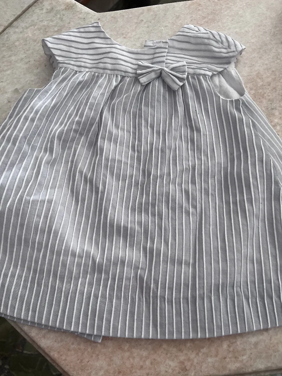 Vestido a rayas grises y blancas, con un lazo en el frente y botones en la espalda. Ideal para niñas.