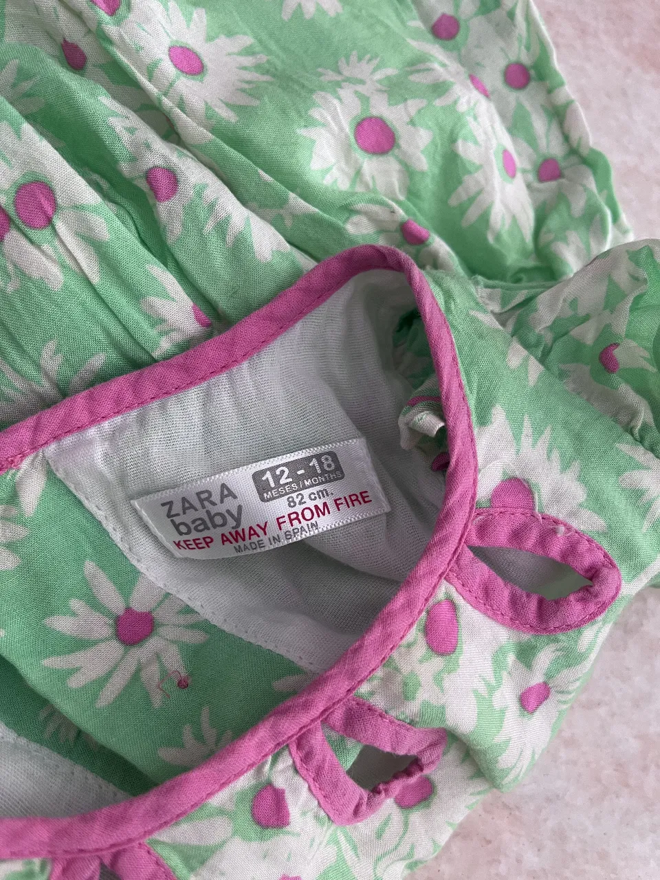 Vestido de verano súper tierno con estampa de flores blancas y fucsia sobre fondo verde. Tiene detalles de volados en las mangas y botones al frente. Ideal para que tu nena juegue y disfrute del sol.