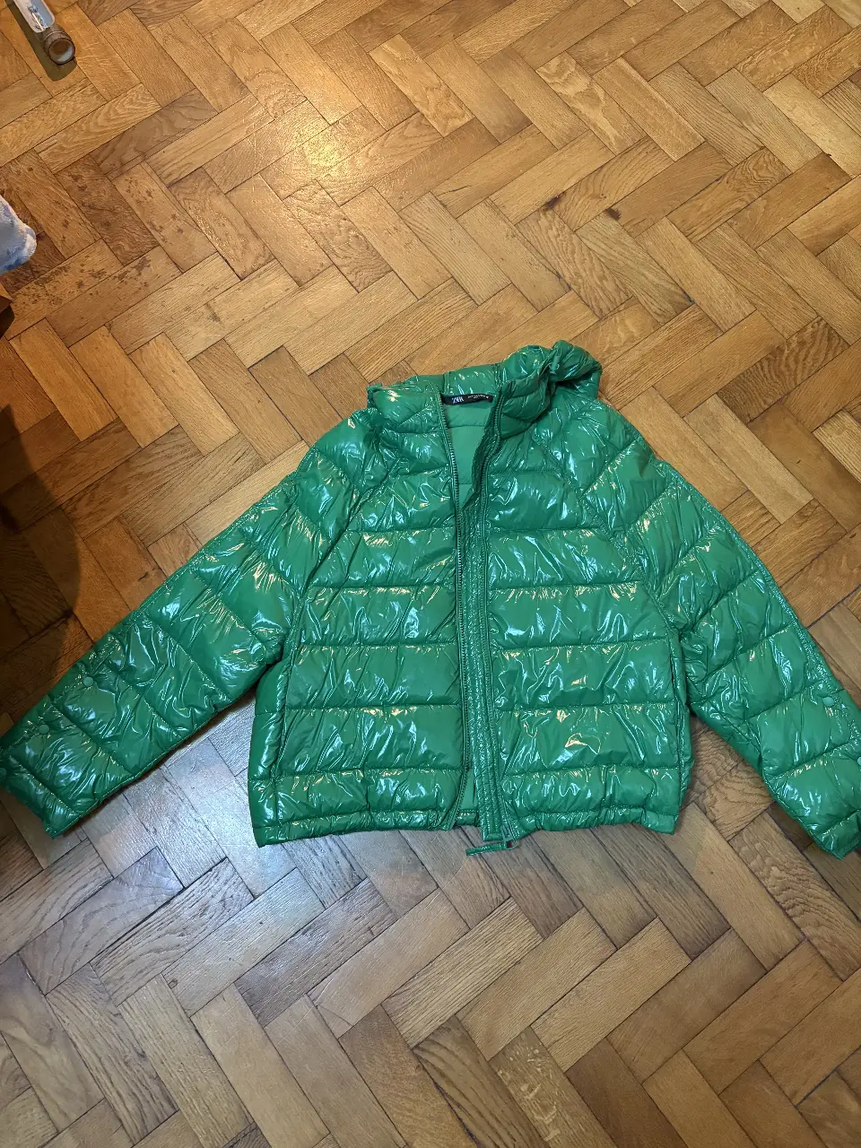 Campera inflable verde brillante de la marca Zara, con capucha y cierre frontal. Ideal para el invierno, esta campera ofrece abrigo y estilo.