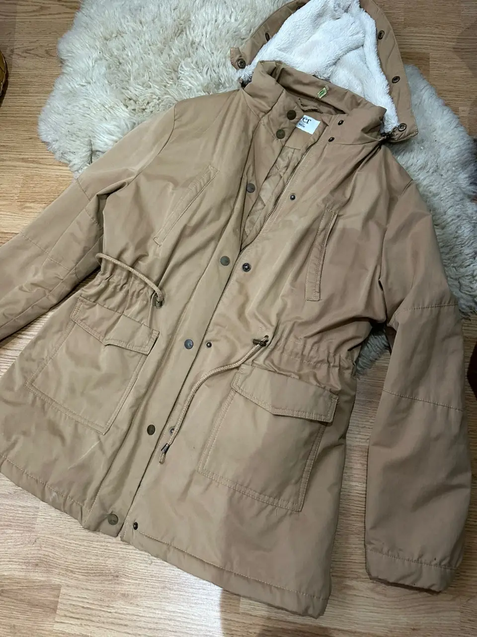 Campera parka de mujer en color camel, con capucha con forro de piel sintética blanca. Posee bolsillos amplios y ajuste en la cintura con cordón. Ideal para el invierno.marca VER