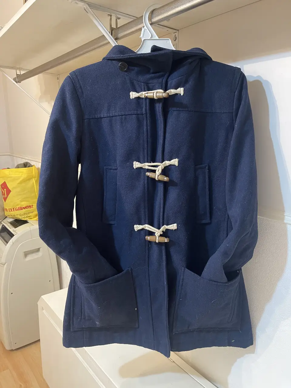 Tapado azul marino con capucha y cierre de botones de madera. Bolsillos delanteros amplios y diseño clásico.