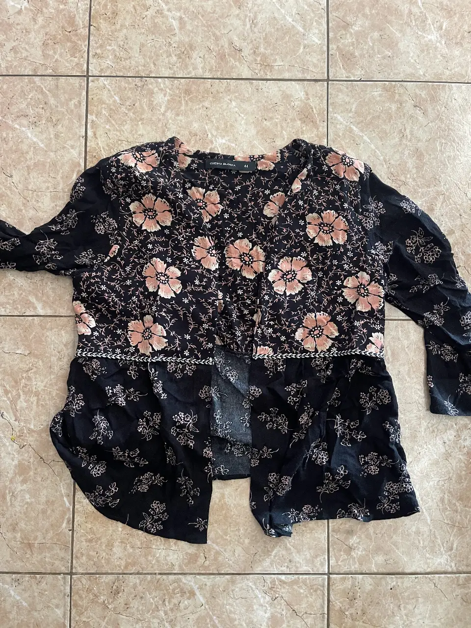 Blusa estampada con flores en tonos rosa y negro. Diseño con botones y detalle de bordado en la cintura. Ideal para un look casual y femenino.