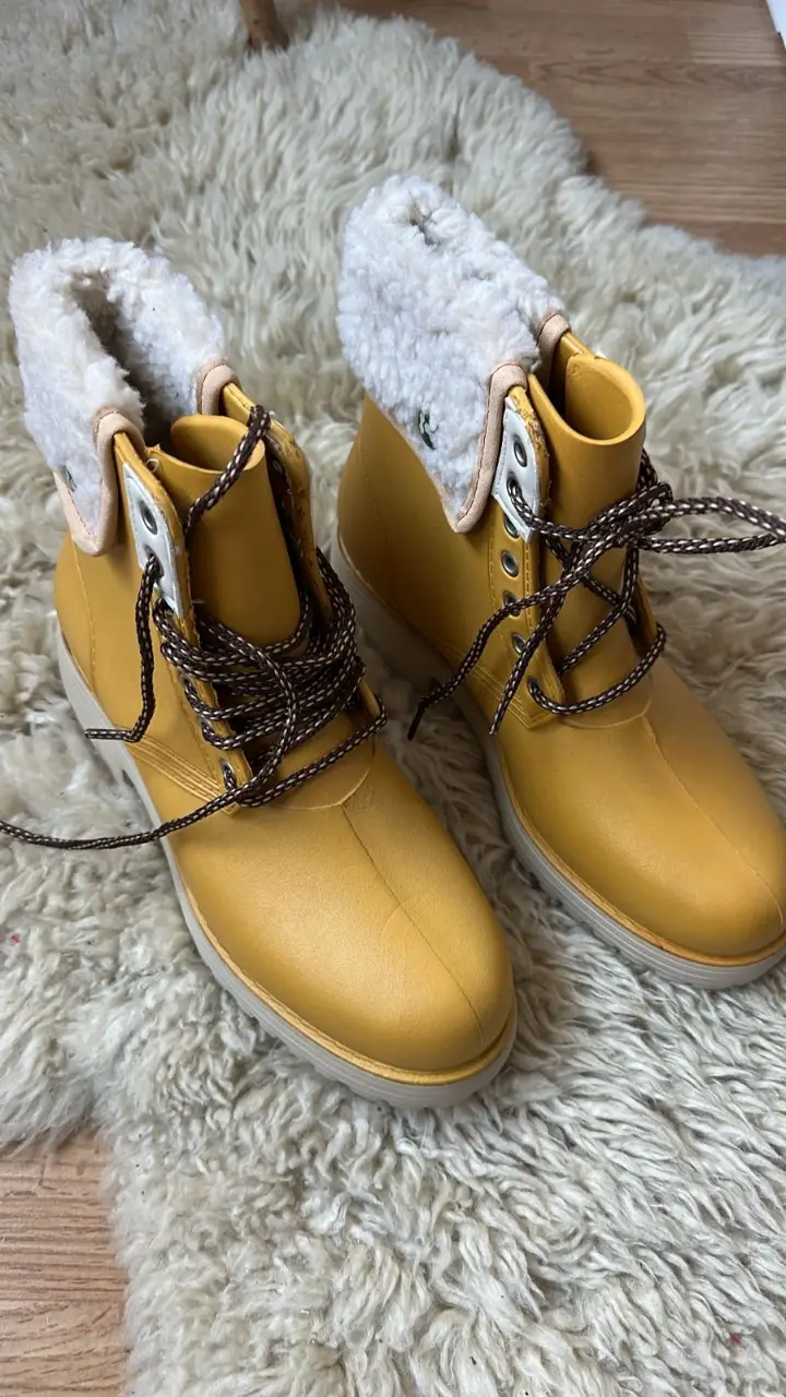 Botas amarillas impermeables con detalle de peluche blanco en el borde superior. Cordones marrones y suela blanca. Ideales para lluvia y un look casual.