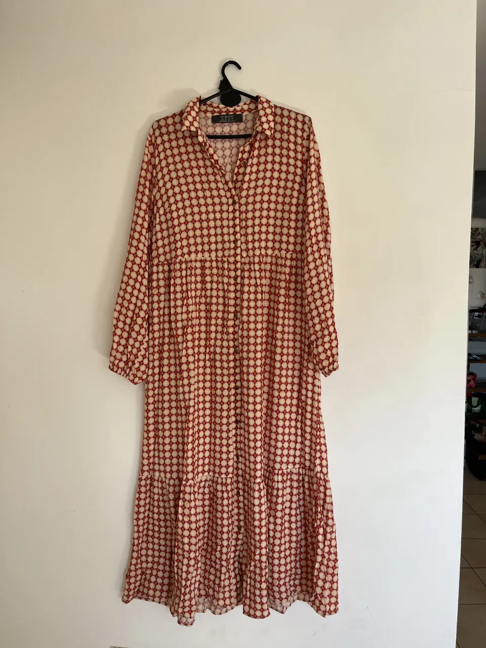 Vestido largo estampado con cuello camisero y botones al frente. Posee mangas largas con puño elastizado y falda con volados. Ideal para un look casual y cómodo.