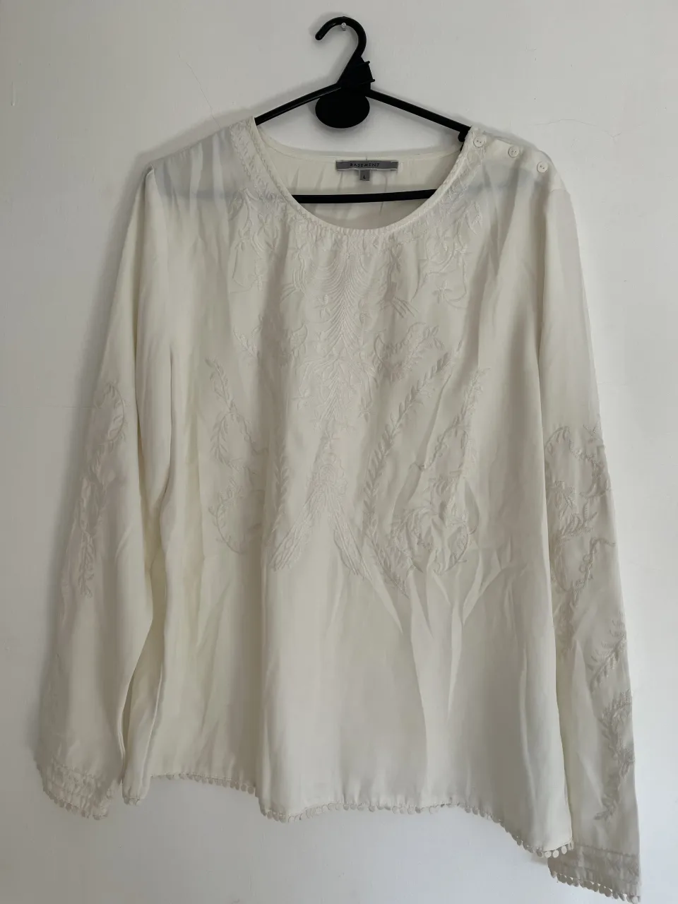 Blusa blanca de manga larga con delicados bordados florales en el frente y las mangas. Posee un detalle de pompones en el borde inferior. Perfecta para un look romántico y casual.