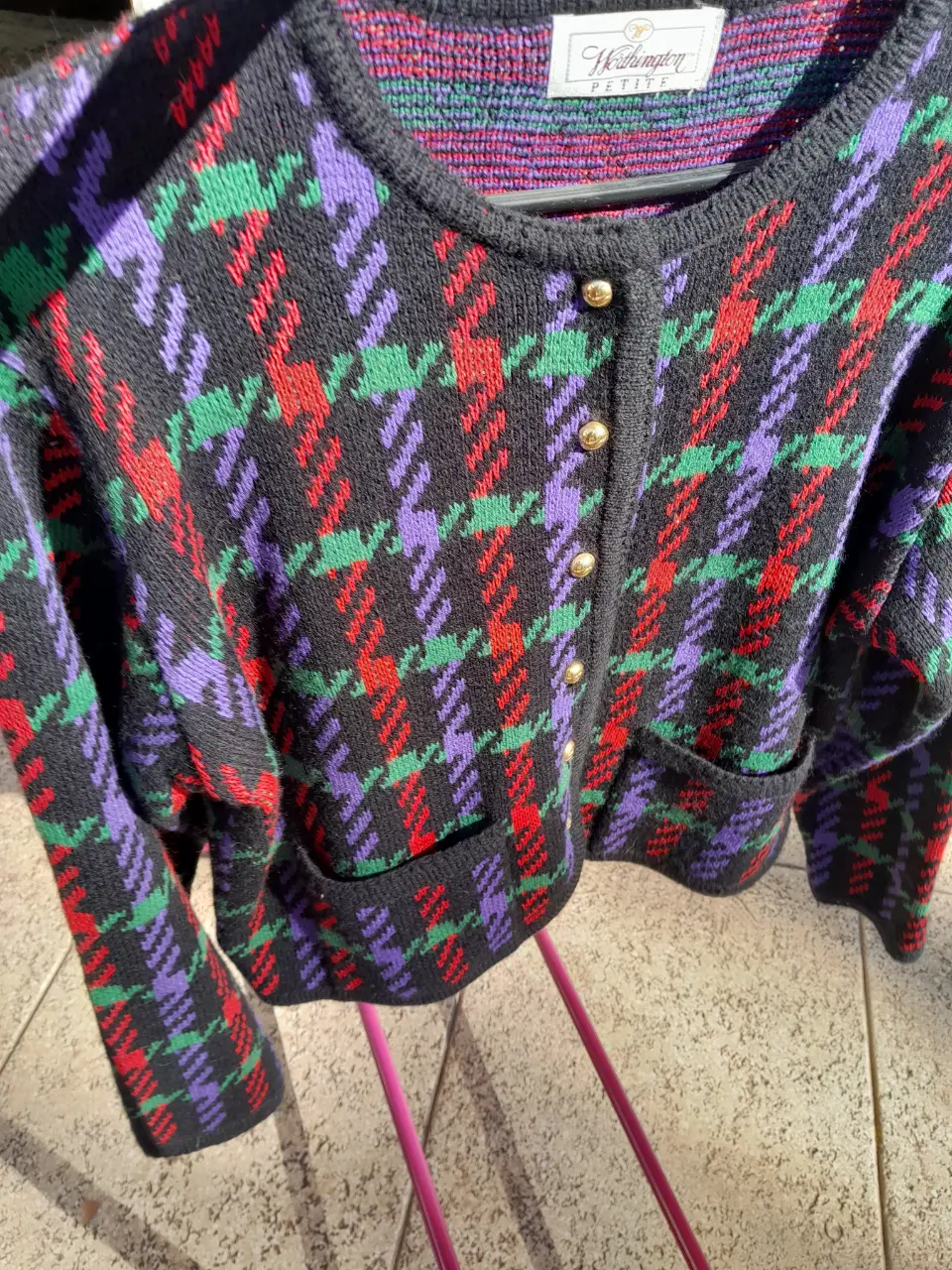 Cardigan vintage con estampado de cuadros en tonos negro, verde, rojo y violeta. Posee botones dorados y bolsillos delanteros. Ideal para un look retro y abrigado.