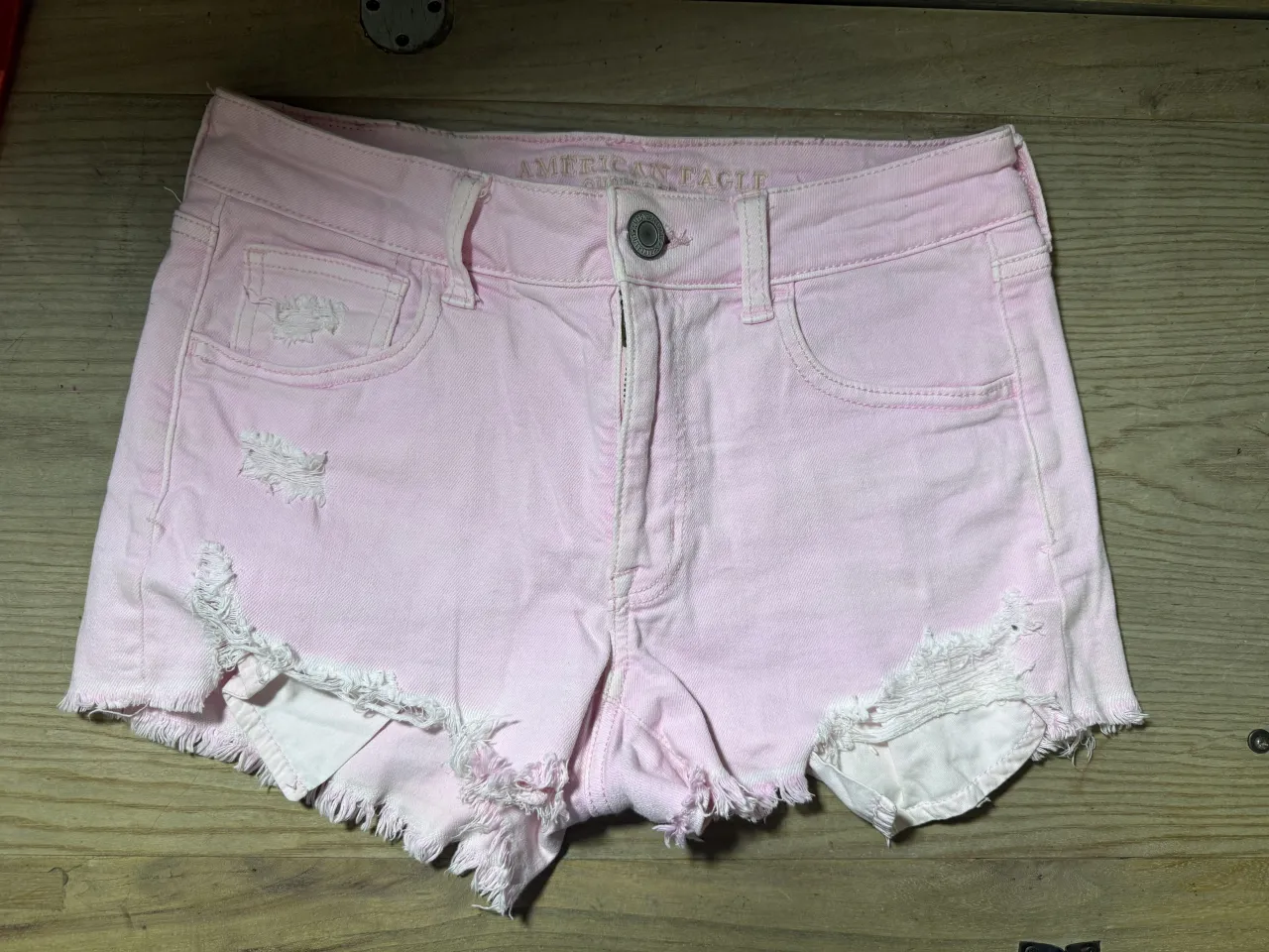 Shorts de jean rosa pálido con roturas y detalles deshilachados en los bordes. Tiro alto, con cinco bolsillos y cierre.