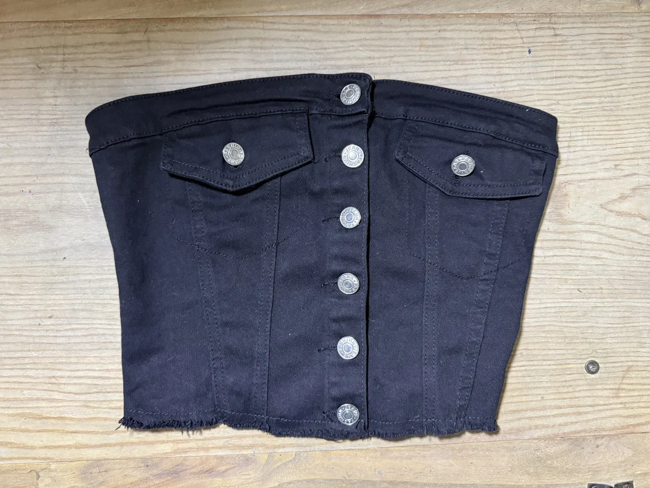 Top de jean negro, súper canchero y moderno. Tiene botones al frente y bolsillos con tapa. El detalle desflecado en la parte inferior le da un toque súper cool. Ideal para combinar con todo y armar looks increíbles.