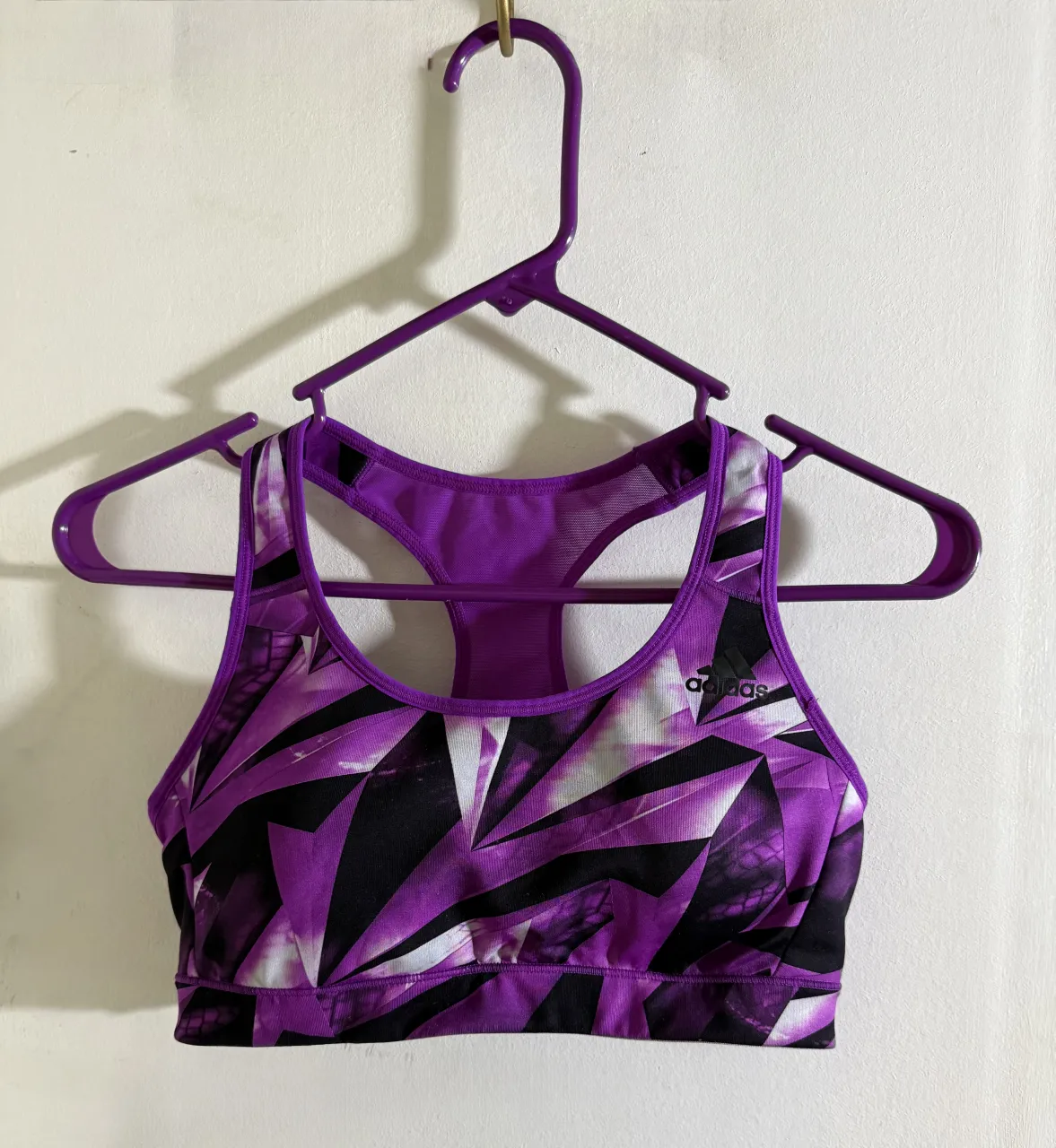 Top deportivo Adidas con estampado geométrico en tonos violeta, negro y blanco. Ideal para entrenamientos o para un look casual y moderno.
