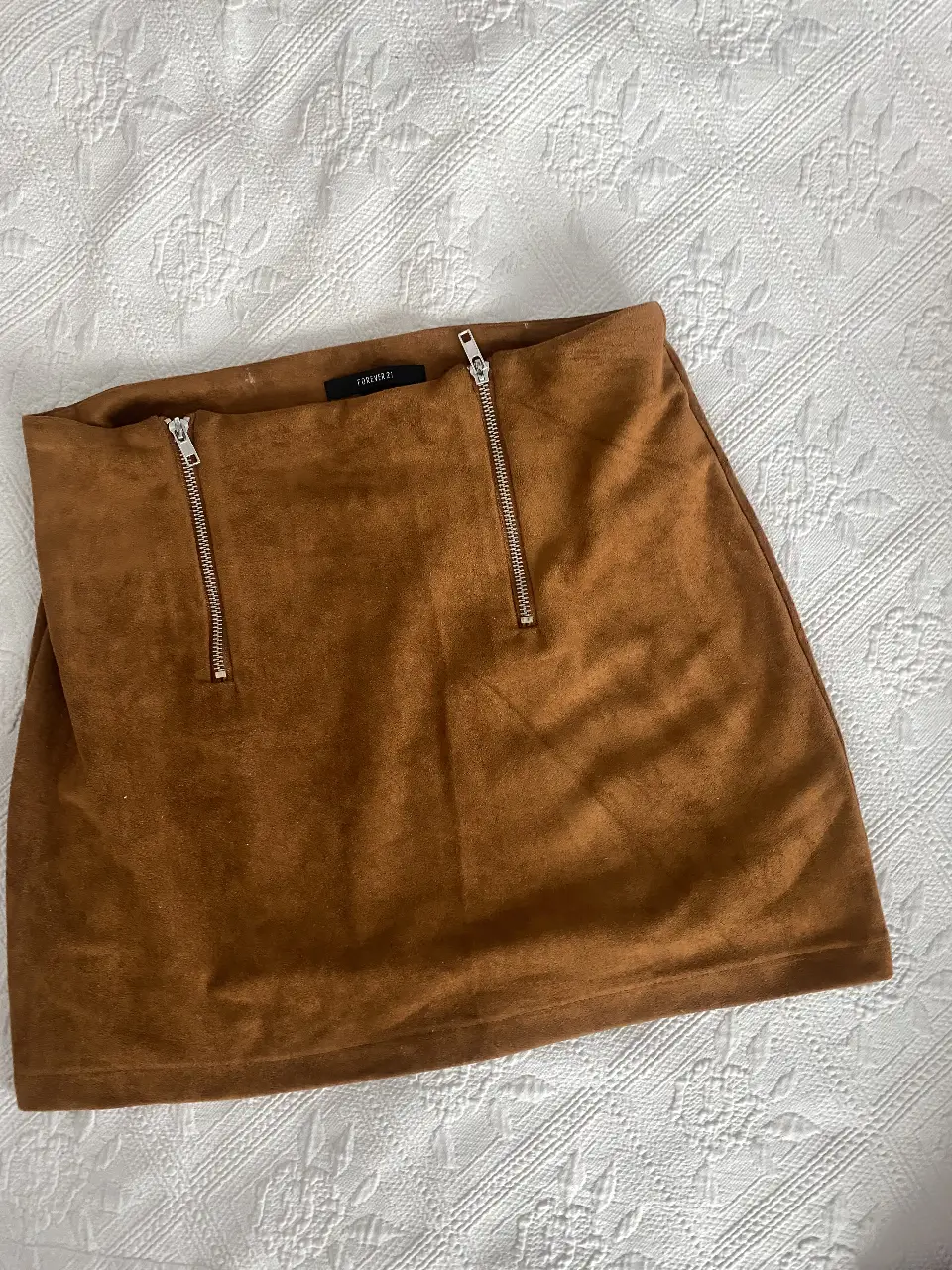 Pollera de gamuza marrón con detalles de cierres. Ideal para un look moderno y sofisticado.