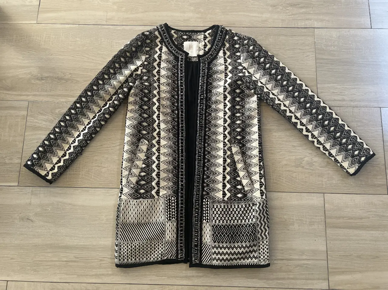 Elegante saco largo con diseño geométrico en blanco y negro. Detalles de pedrería en el cuello y bordes. Ideal para un look sofisticado y versátil.