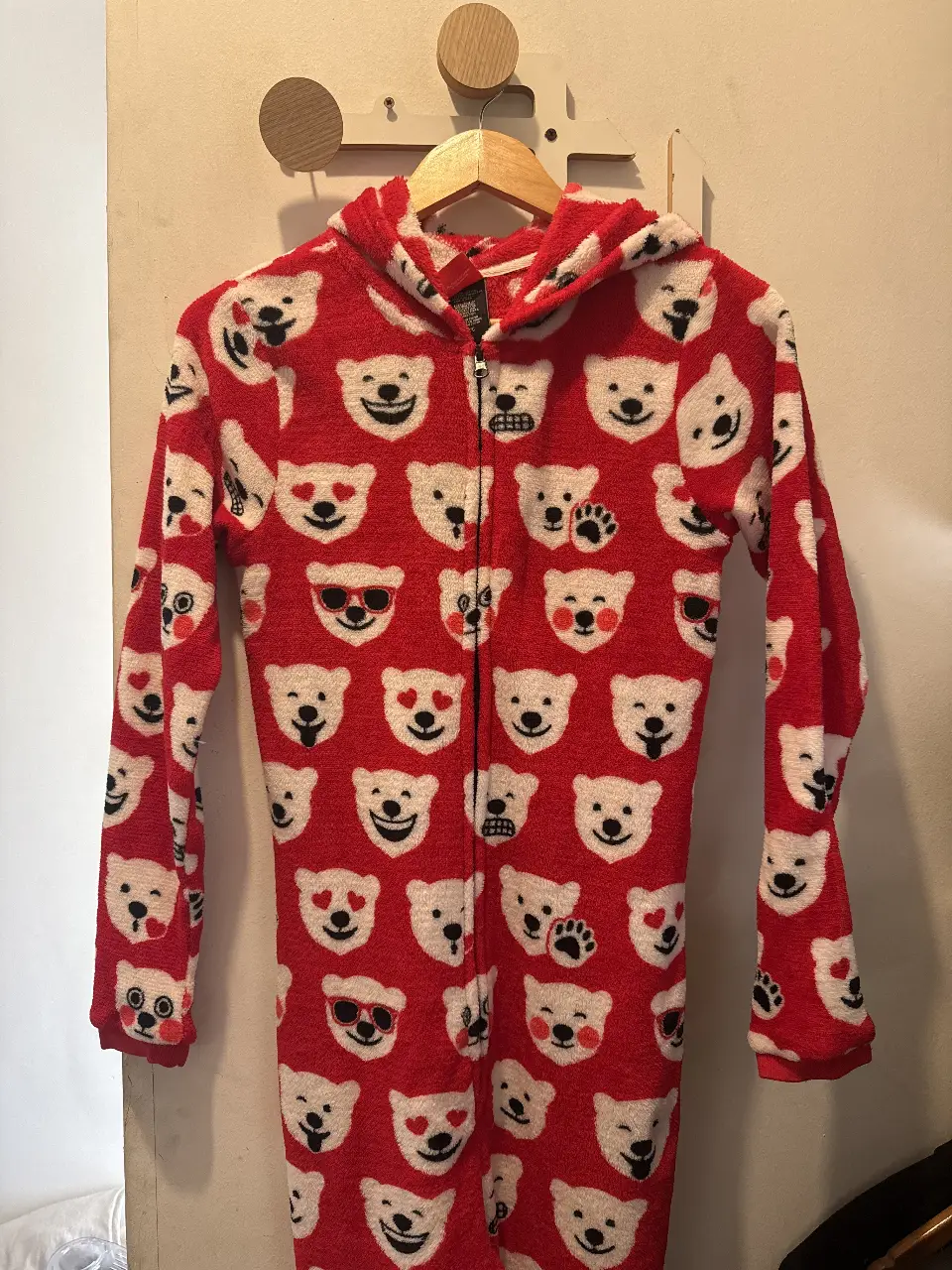 Enterito pijama de polar rojo con estampado de caritas de osos polares. Tiene capucha y cierre frontal. Ideal para estar cómodo en casa.