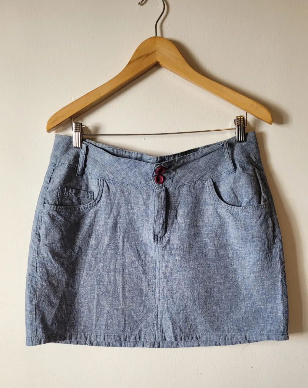 Pollera corta de jean color azul con dos botones y cierre al frente, bolsillos delanteros y traseros.