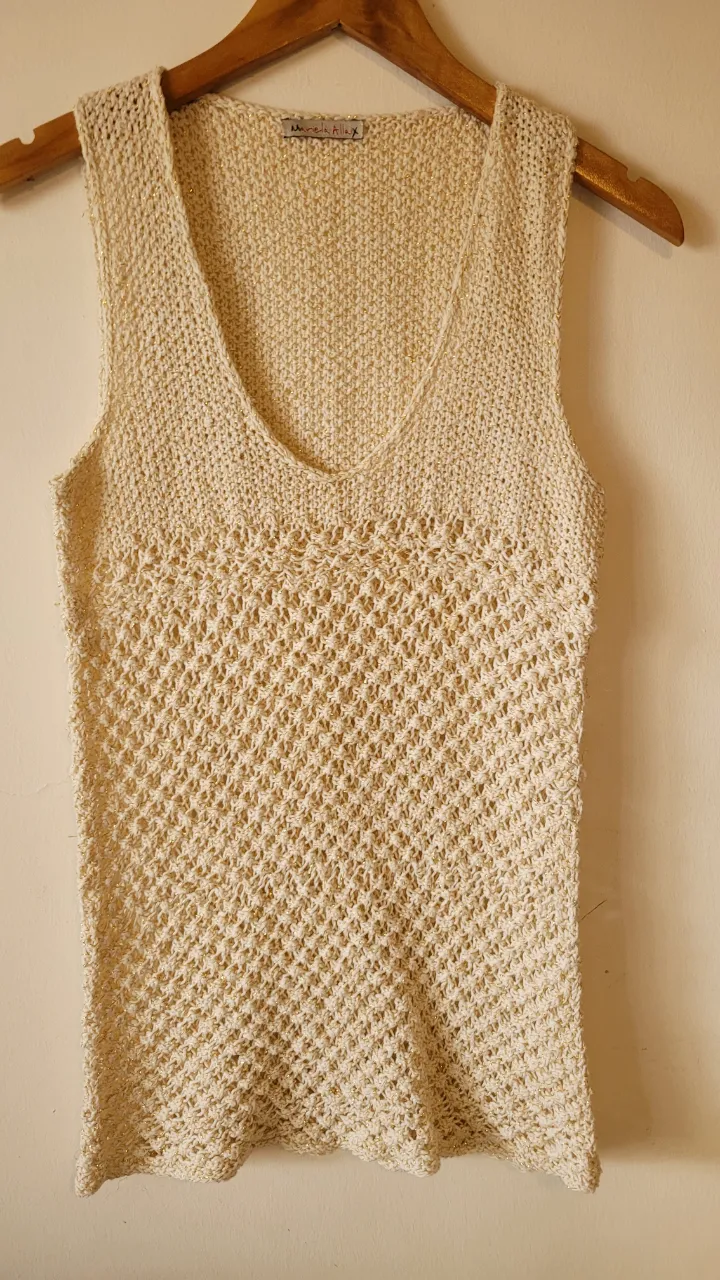 Musculosa tejida color crudo con detalles dorados. Posee un tejido calado en la parte inferior y un tejido más cerrado en la parte superior.