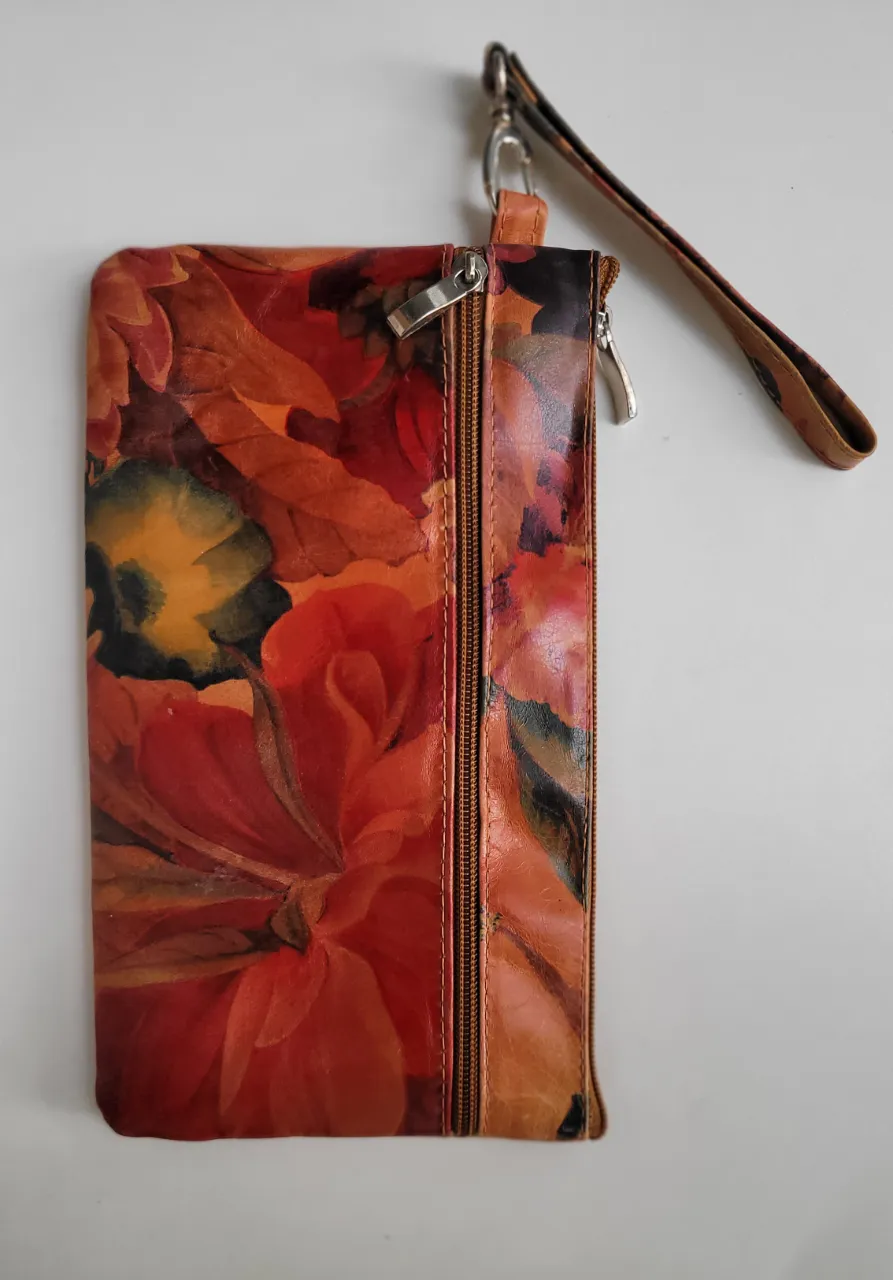 Cartera tipo clutch con estampa floral en tonos tierra, ocres y rojizos. Posee cierre principal y un bolsillo exterior con cierre. Incluye tira de mano. Impecable. Poco uso.