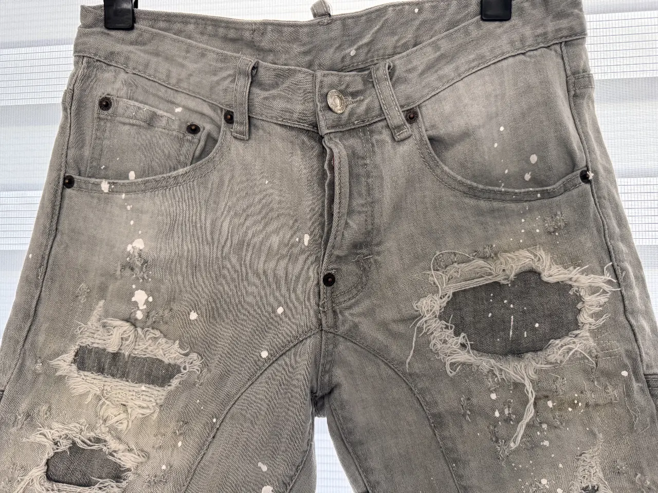 Short de jean gris con roturas y detalles de pintura blanca. Diseño Dsquared2, estilo urbano y moderno, ideal para un look casual y con onda.