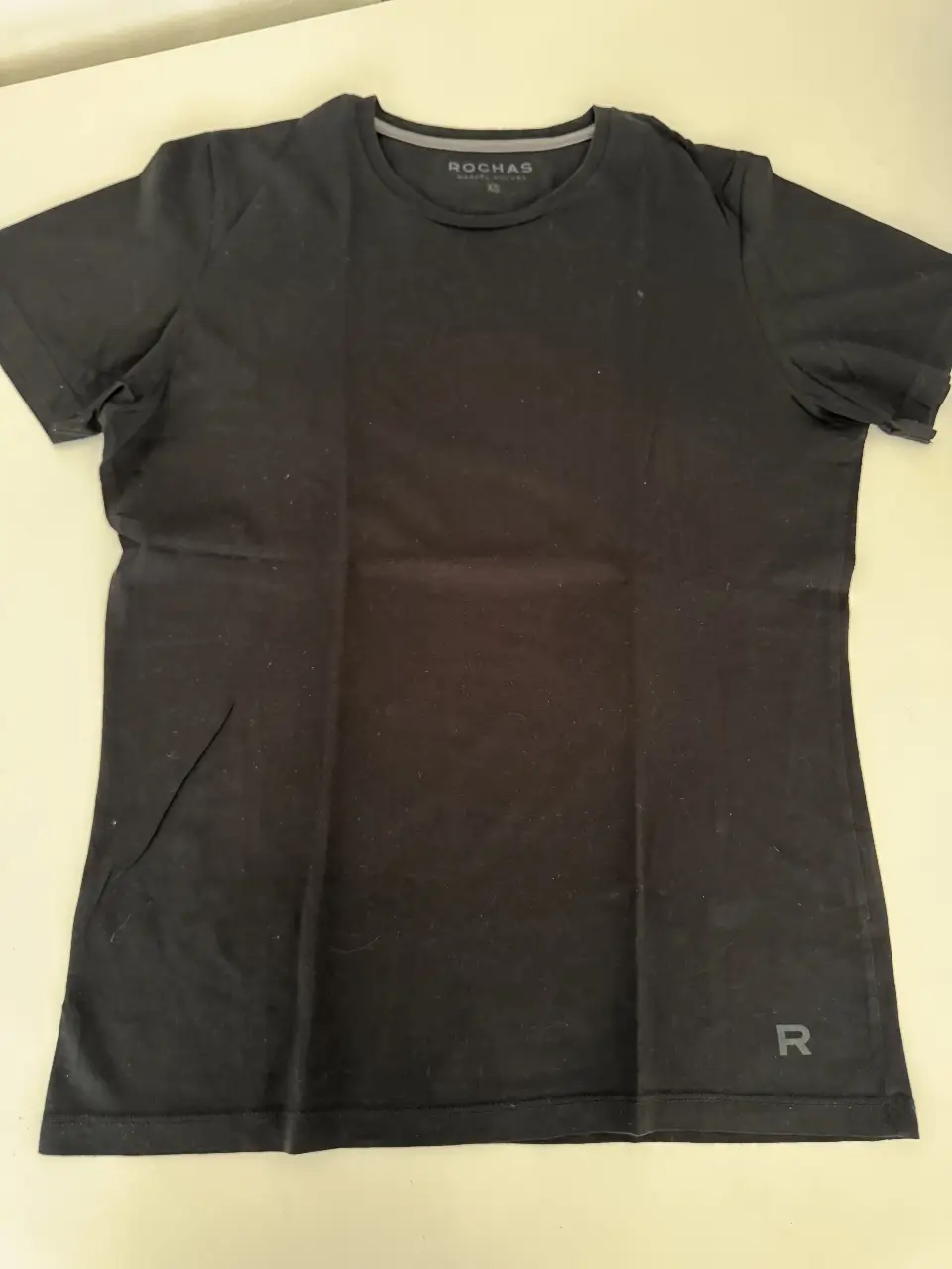 Remera negra de hombre, de manga corta, con cuello redondo y logo de la marca Rochas. Ideal para un look casual y cómodo.