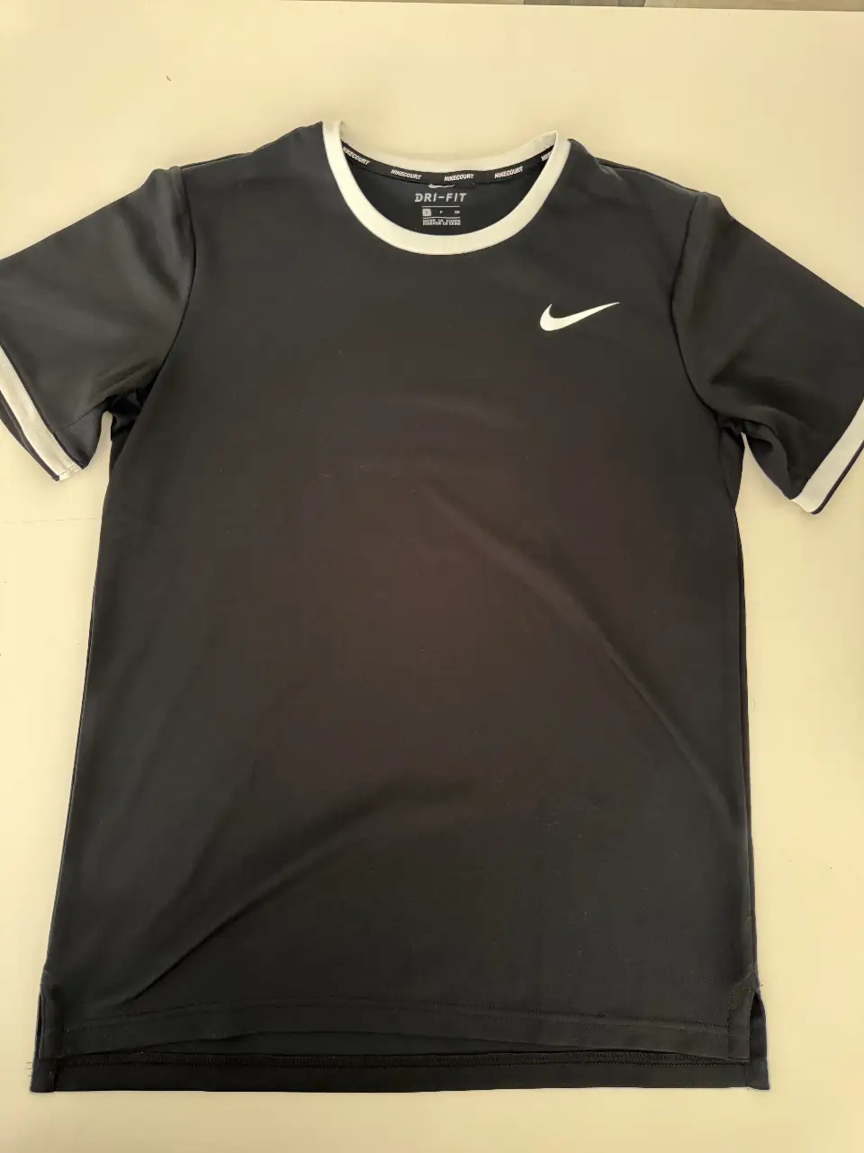 Remera deportiva Nike Dri-FIT para hombre, de color negro con detalles blancos en cuello y mangas. Logo de la marca en blanco. Ideal para entrenamientos y actividades físicas.