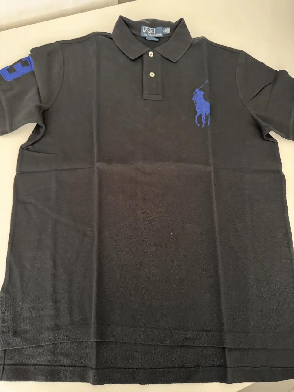 Remera polo negra de hombre, con el logo de Polo by Ralph Lauren en azul en el pecho y el número 3 en la manga izquierda. Ideal para un look casual y elegante.