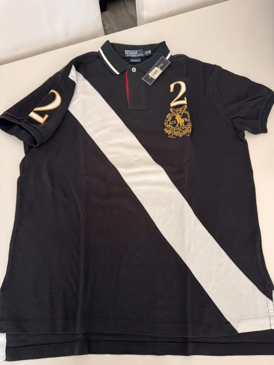 Remera polo de hombre, negra con detalle blanco diagonal y número 2 en dorado. Marca Polo by Ralph Lauren, Custom Fit. Ideal para un look deportivo y casual.