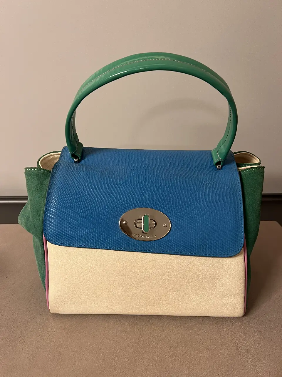 Cartera Jackie Smith de cuero, con solapa azul y manija verde. Diseño tricolor con detalles en rosa y cierre metálico.