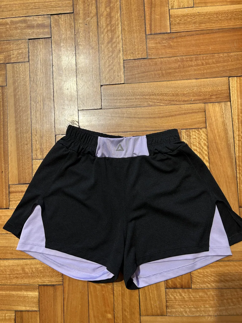 Shorts deportivos negros con detalles en lila. Ideales para entrenar o para un look casual y cómodo. Tienen un diseño de doble capa y cintura elastizada.