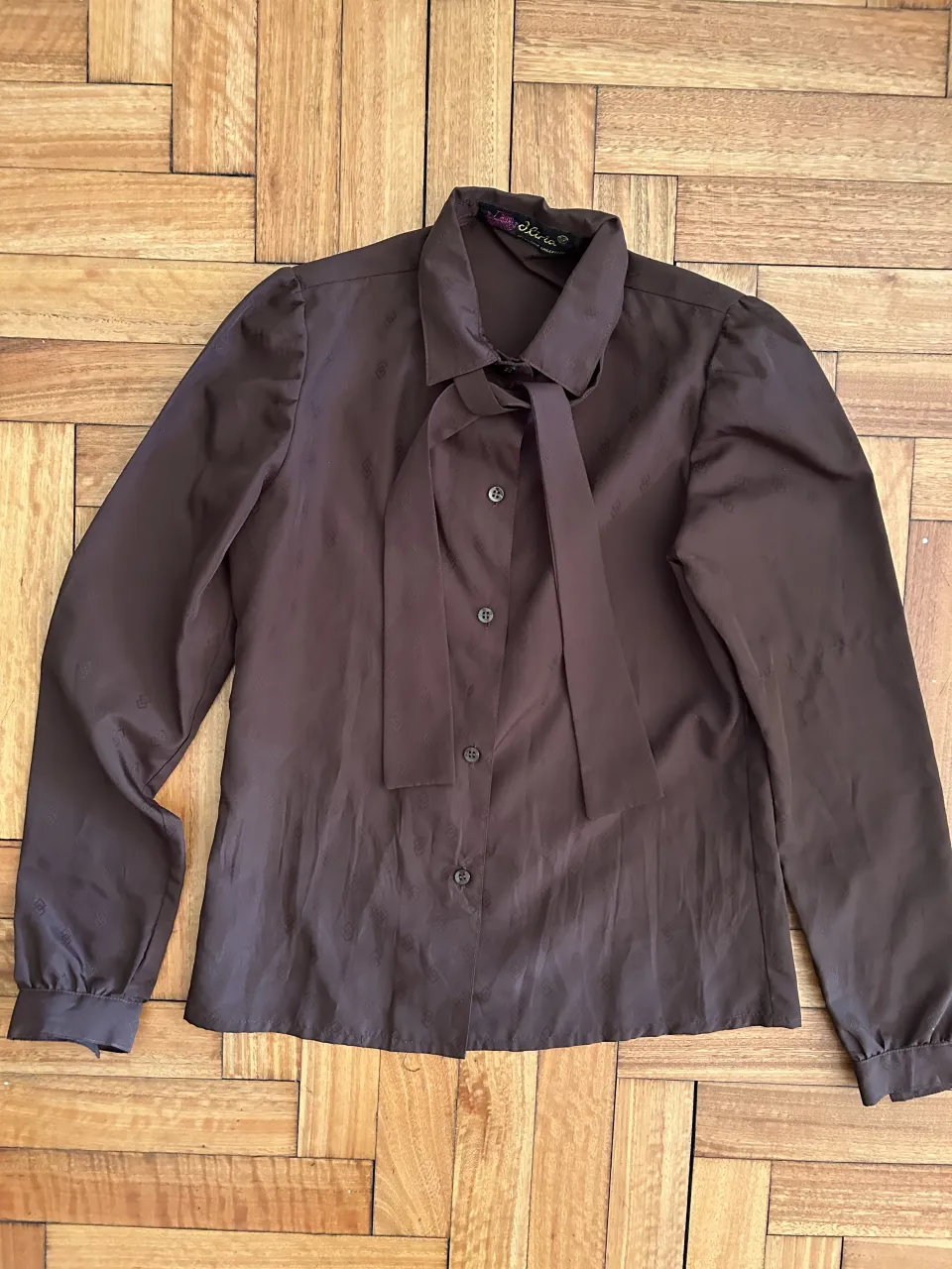 Camisa marrón de vestir con cuello mao y lazo. Posee un estampado sutil de rombos en toda la tela. Ideal para un look elegante y formal.