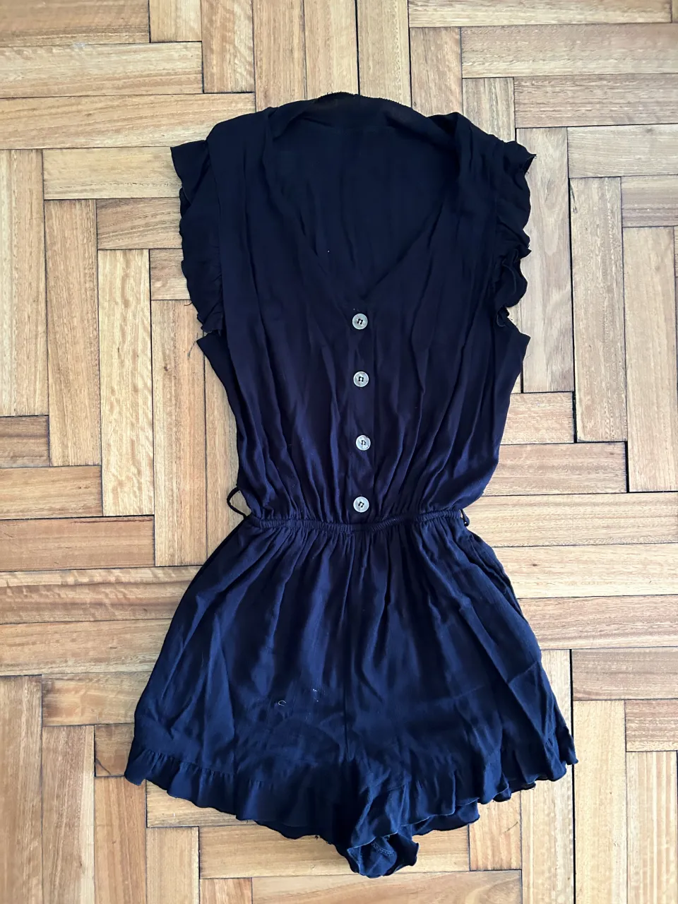 Mono negro corto con volados en mangas y ruedo. Tiene botones al frente y cintura elastizada con detalle de lazo.