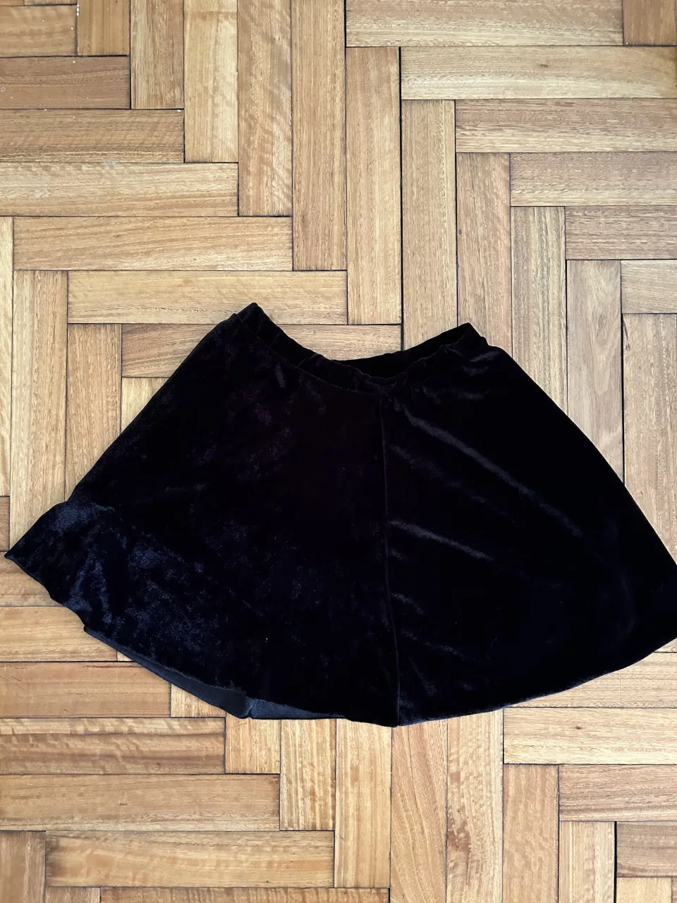 Pollera negra de terciopelo, con un corte acampanado y detalles de satén en el borde. Ideal para un look elegante y sofisticado.