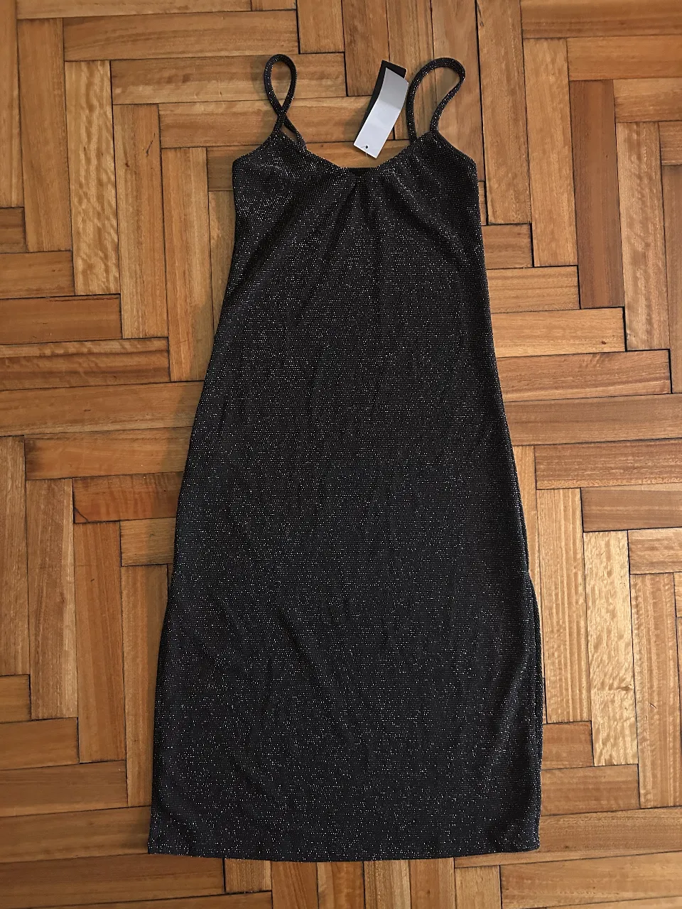 Vestido de lurex negro con brillos, ideal para fiesta o salida. Con tirantes finos y un corte ajustado, este vestido es perfecto para lucir un look elegante y moderno.