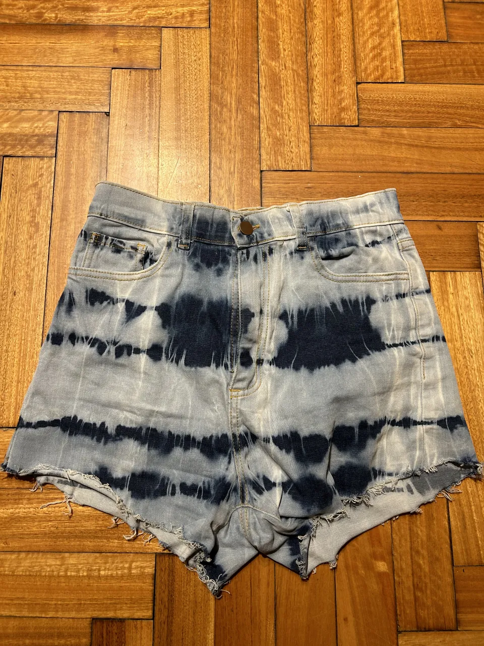 Shorts de jean tiro alto con efecto tie-dye en tonos azules y blancos. Tienen roturas y un estilo desgastado.