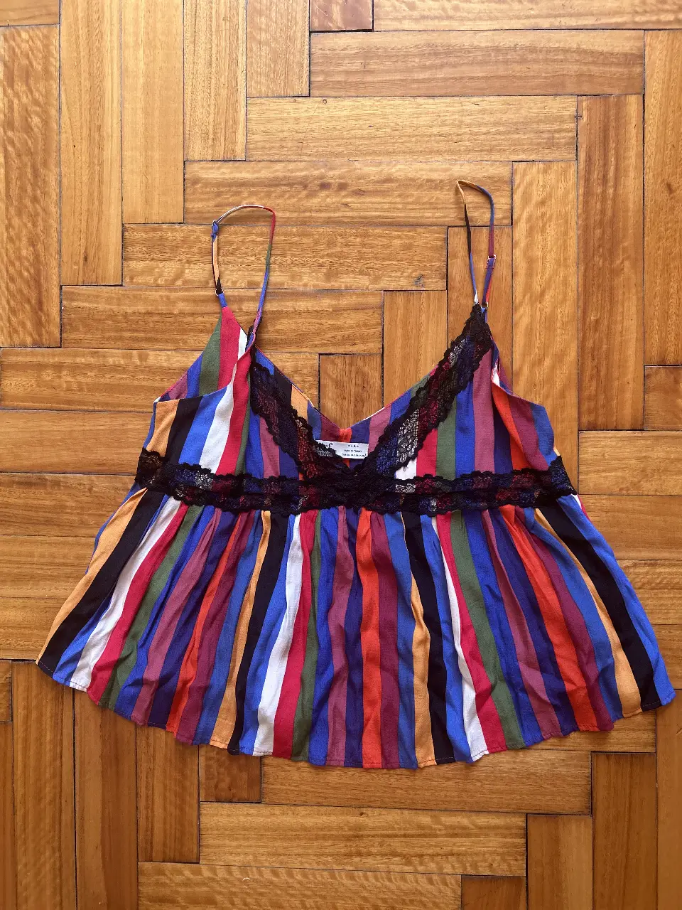 Top de mujer con diseño a rayas verticales multicolores. Tiene detalles de encaje negro en el escote y en la parte inferior. Ideal para un look fresco y moderno.