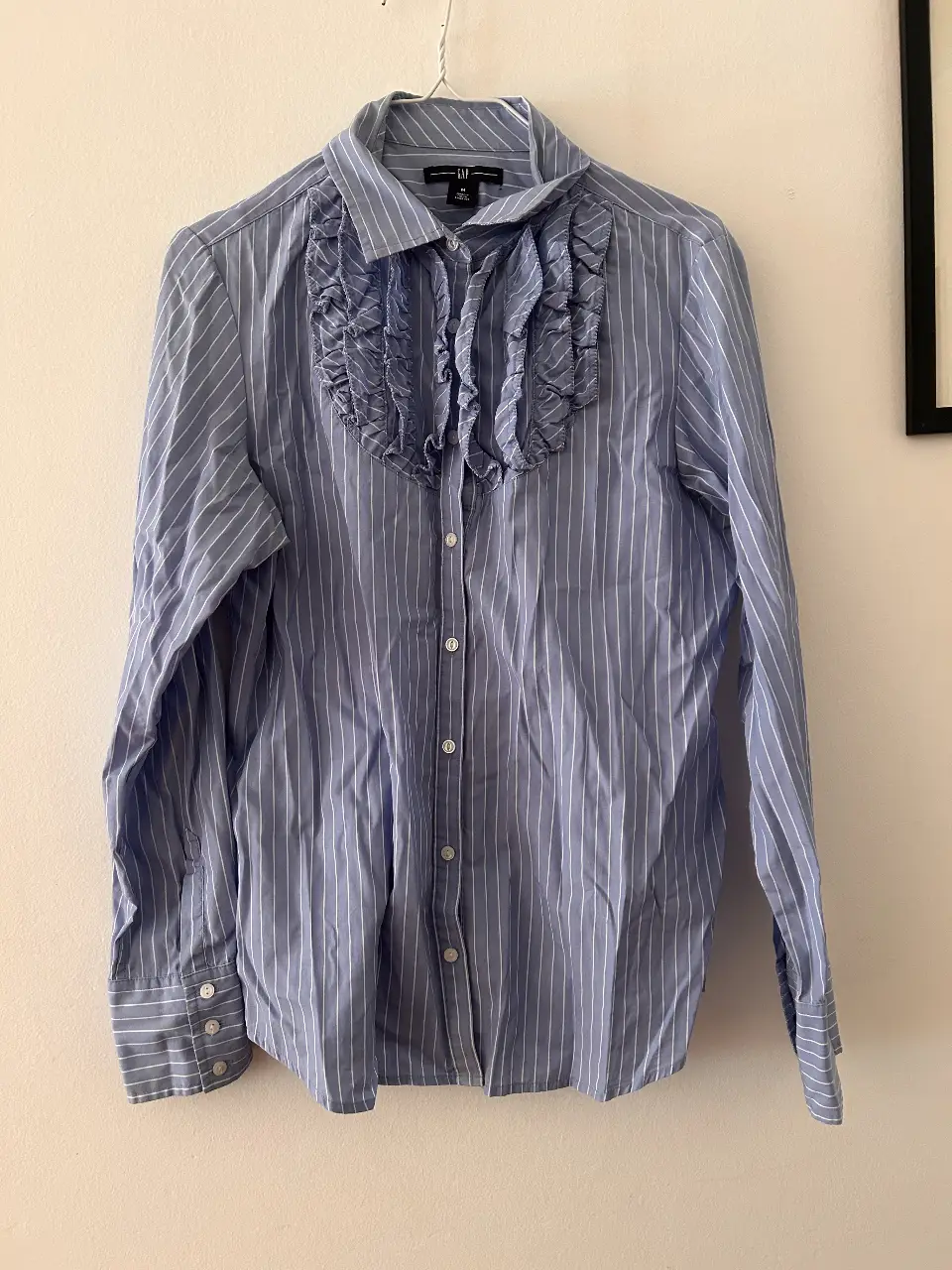 Camisa de mujer a rayas celeste y blanca de la marca GAP, con detalle de volados en el cuello. Ideal para un look casual y elegante.