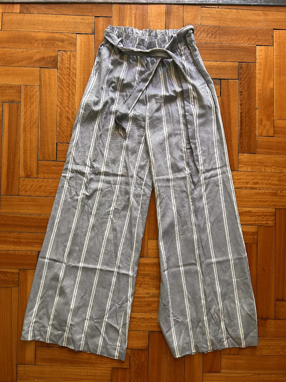 Pantalón suelto de mujer, con rayas verticales en gris y blanco. Talle 36 con cintura elastizada y lazo para ajustar. Ideal para un look casual y cómodo.