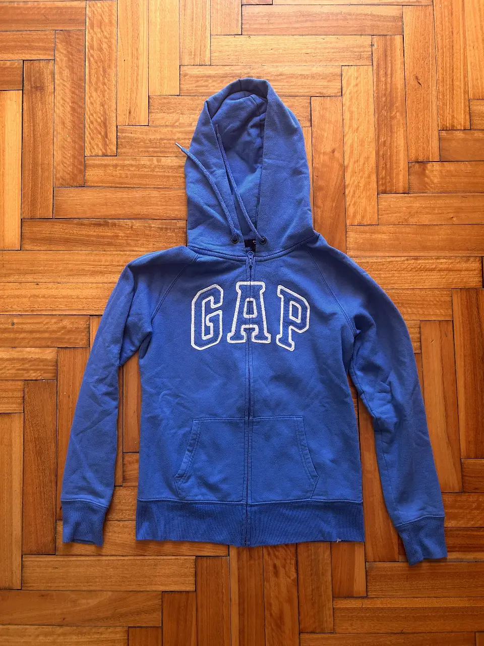 Buzo con cierre de la marca GAP, de color azul, con capucha y bolsillo tipo canguro. Ideal para un look casual y cómodo.
