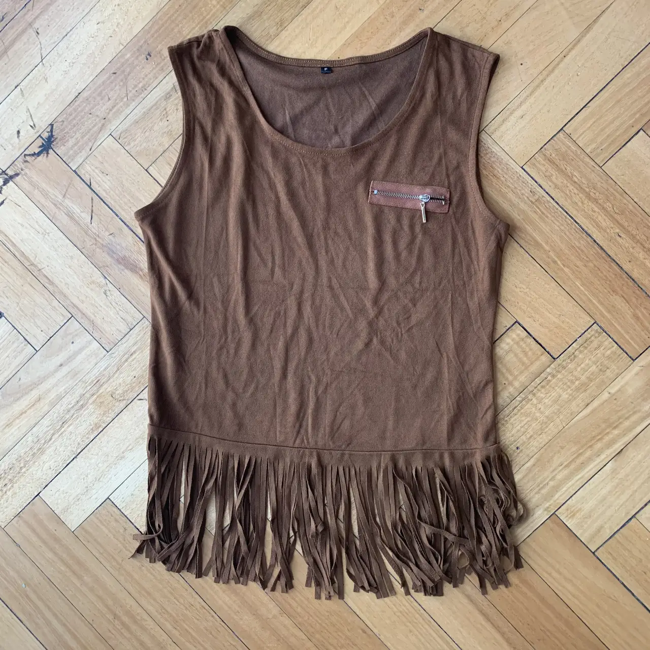 Musculosa marrón con flecos en el bajo y detalle de bolsillo con cierre en el pecho. Ideal para un look bohemio y casual.