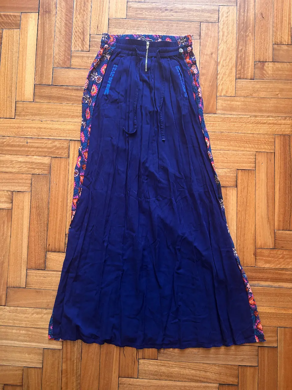 Pollera larga de mujer, con cintura elastizada y cierre. Diseño con detalles florales en los laterales y en la cintura. Ideal para un look bohemio y fresco.