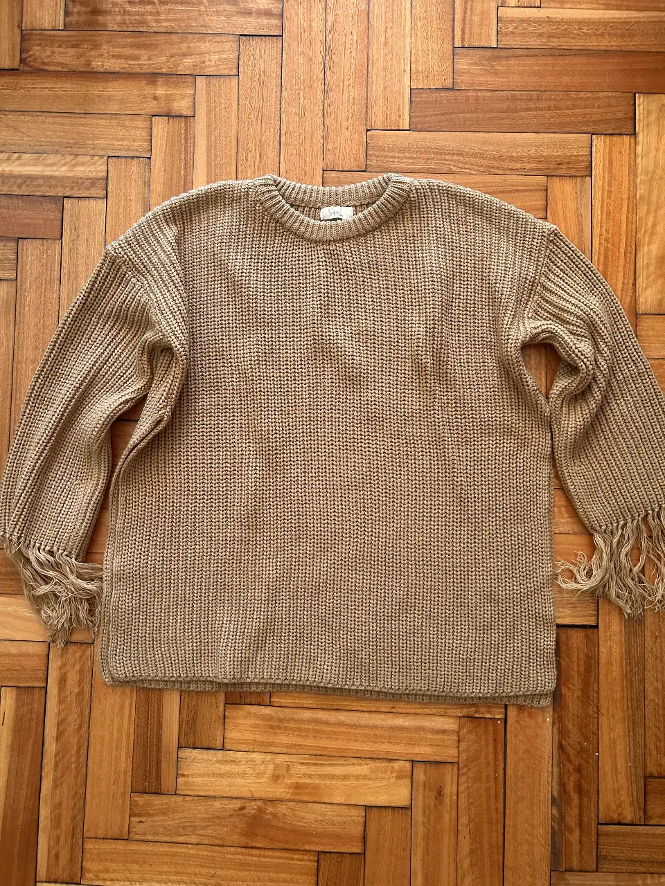 Sweater de punto color marrón con flecos en las mangas. Cuello redondo y corte holgado. Ideal para un look casual y cómodo.