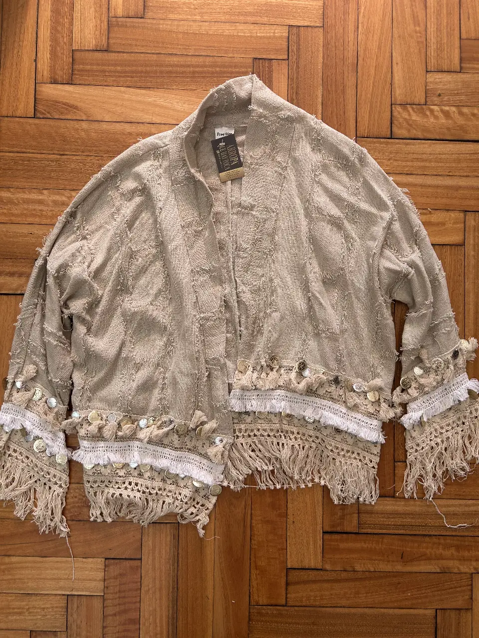 Kimono artesanal de tela rústica color crudo, con detalles de encaje, flecos y lentejuelas. Ideal para un look boho chic.
