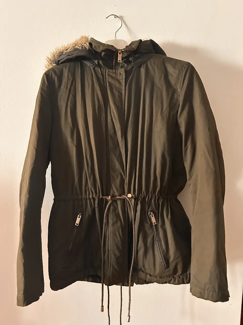Campera parka verde oscuro con capucha y forro de piel sintética marrón. Posee bolsillos con cierre y ajuste en la cintura con cordón. Ideal para el invierno.