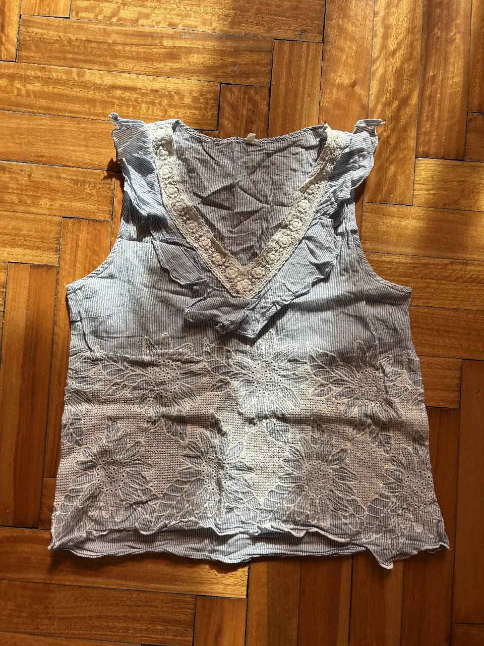 Blusa de mujer con diseño floral bordado en la parte delantera y detalles de encaje en el cuello. Confeccionada en tela a rayas azul y blanca, ideal para un look fresco y casual.