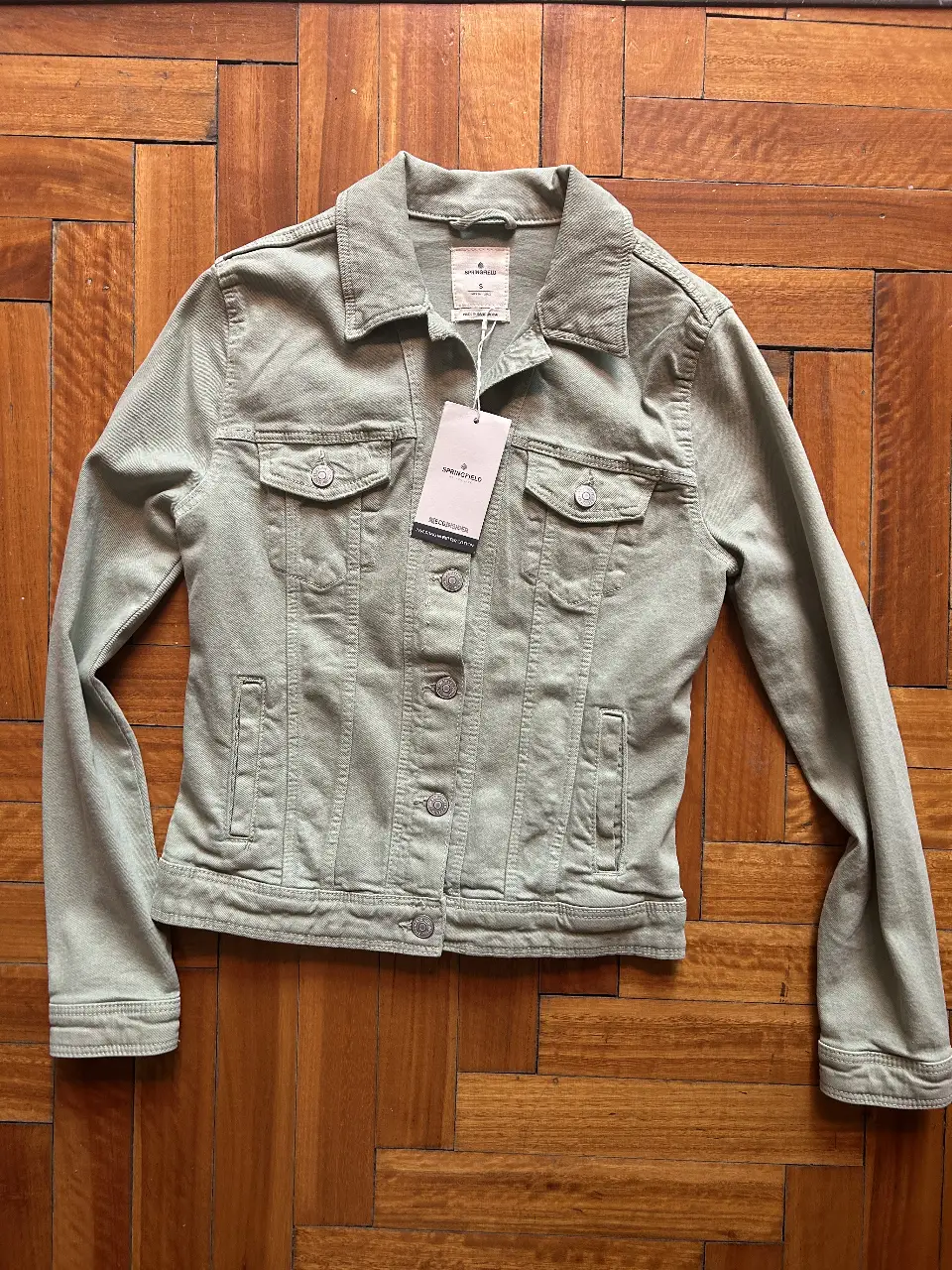 Campera de jean de mujer en color verde claro, con un diseño clásico de corte entallado. Cuenta con dos bolsillos en el pecho y dos laterales, cierre con botones y cuello camisero. Ideal para un look casual y moderno.