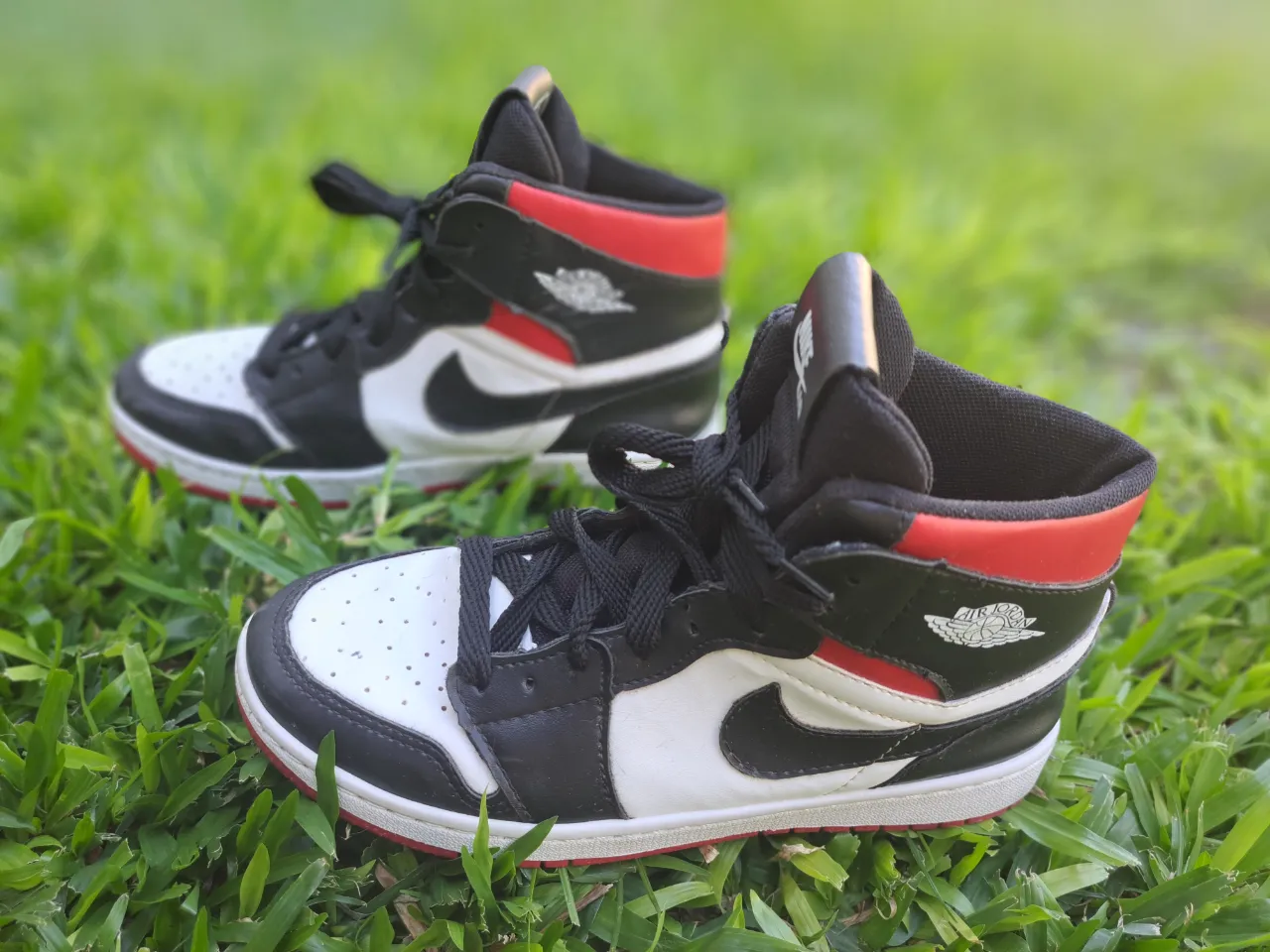 Zapatillas Nike alta con cordones, combinando paneles blancos, negros y detalles en rojo. Presentan el logo de Nike Air en la lengüeta y el logo de Jordan en el lateral.  Muy buen estado